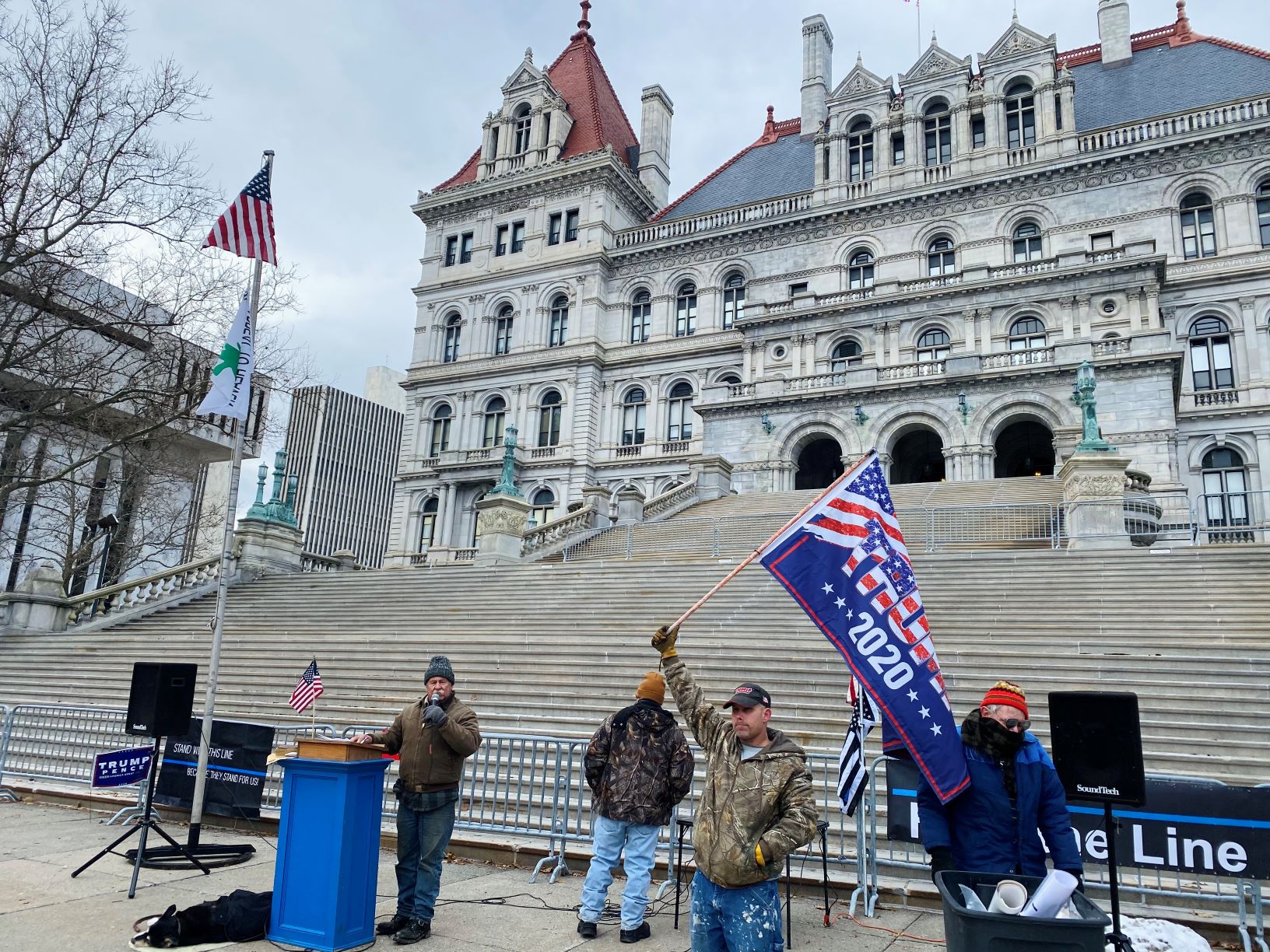 12月26日，紐約州首府奧爾巴尼（Albany）州府議會大廈（East Capitol Park）前，多位民眾揭露中共罪行，打旗者為John。